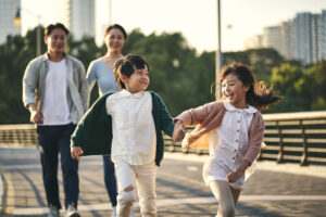 happy asian family with two children walking on pedestrian bridge in city park