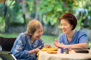 Elderly woman with caregiver in the needle crafts occupational therapy for Alzheimer’s or dementia